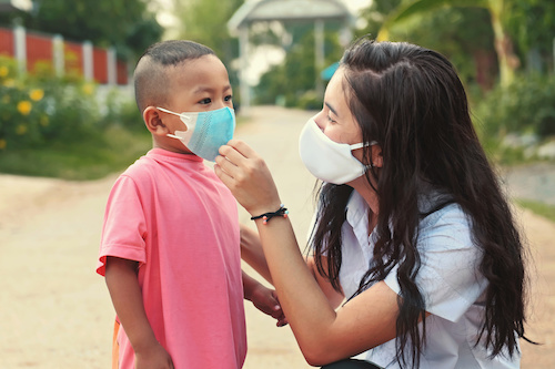 Mother helping child put on face mask to protect from COVID-19