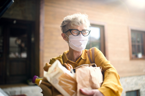 Senior woman wearing face mask who is receiving bagged groceries
